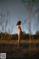 A naked woman standing in the middle of a field.