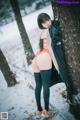 A woman leaning against a tree in the snow.